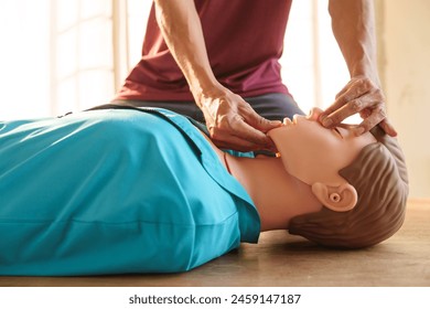 Close-up of middle-aged Asian male hands performing cardiopulmonary resuscitation (CPR) on a training dummy. Vital techniques include defibrillation, chest compressions, and maintaining the airway. - Powered by Shutterstock