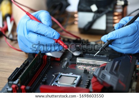 Close-up of middle-aged man measuring electrical voltage. Technician male repairing computer mainboard using digital multimeter. Technology and diy concept