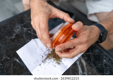 Close-up of a middle-aged mans hands using an herb grinder to prepare cannabis on a marble table, highlighting a therapeutic ritual that blends recreational and medicinal cannabis use. 
