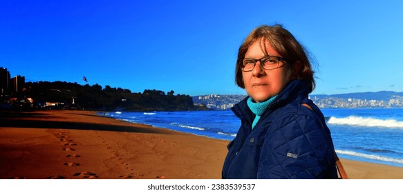 Close-up of middle-aged woman with intense gaze, on the beach at sunset, intense colors, blue sky - Powered by Shutterstock