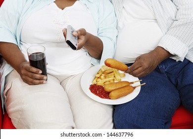 Closeup midsection of an overweight couple with junk food holding remote control