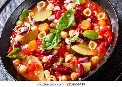 Close-up Of Minestrone Soup With Red Beans, Zucchini, Garbanzo Beans, Small Pasta Shells, Cheese, Tomato, Carrots And Basil In Black Bowl