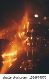 A Closeup Of Mini Disco Balls Under Red And Orange Lights With A Blurry Background