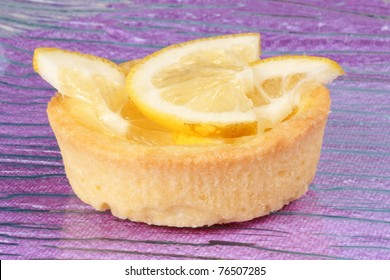 Closeup Of A Mini Lemon Fruit Tart On A Glass Plate Over A Pink Background. With Copy-space. Selective Focus.