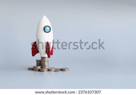 Close-up of miniature rocket stand on stack of coins, rocketship as symbol to open business project or startup. Success, growth, career concept. Copy space