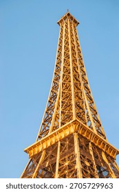 close-up minimalist view from below of Eiffel Tower parody top against blue sky lit by sunlight