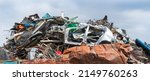 Close-up of mixed scrap metal pile in junkyard on panoramic blue sky background. Colored jumble of iron waste as old car body, wire mesh or rusty sheet and various leftover recyclable materials. Dump.