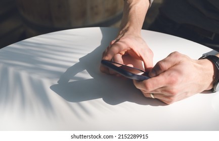 Close-up Of Mobile Phone In Hands On White Table. Sunlight.