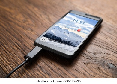 Close-up Of Mobile Phone With Low Battery Symbol On Charge