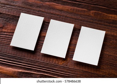 Closeup Mockup Of Three Blank Vertical Business Cards At Brown Wooden Table Background.