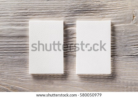 Closeup mockup of two blank vertical business cards at light natural wooden background.