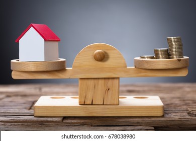 Closeup of model home and coins balancing on wooden weighing scale