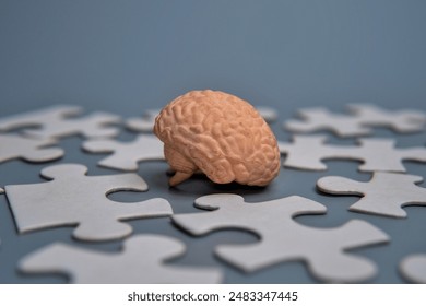 A close-up model of a human brain surrounded by scattered puzzle pieces.