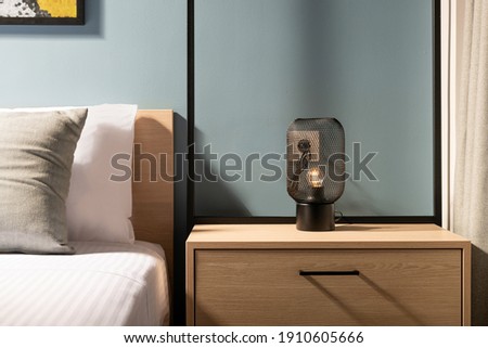 Closeup of modern black metal edison bulb lamp on wooden bedroom night table in contemporary style gray room interior with pine wood bed and white cotton bedlinen