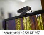 Close-up of a modern black USB webcam mounted on a computer monitor with a blurred indoor background, representing remote work and online communication.