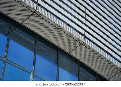 A close-up of a modern building facade combining perforated metal panels and reflective glass, showcasing sleek architectural details.