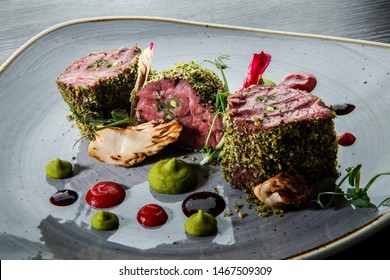 closeup modern decorated three raw baked meat pieces served with assorted sauces on modern restaurant plate on wooden table
