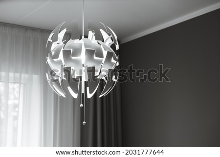 Close-up of modern designed chandelier with burning lamp. Contemporary interior of livingroom or bedroom. Black and white.