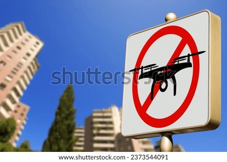 Close-up of a modern drones prohibited sign (road sign of no fly drones area) against a clear blue sky in a city with blurred residential buildings, photography.