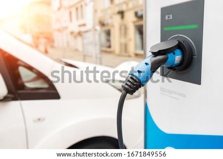 Close-up modern electric commercial van car plugged with fast charger at charging station in center of old European city. Eco friendly green energy vehicle. Zero emission transport