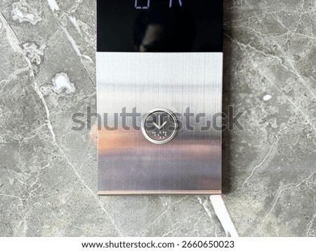 A close-up of a modern elevator button panel with a downward arrow, set against a luxurious marble wall. Perfect for concepts of technology, urban life, and modern architecture