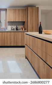 Close-up of a modern kitchen interior featuring light wooden cabinets, a central island, and a wine bottle. Clean, minimalist design