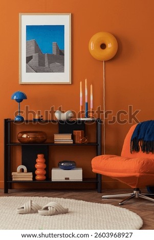 Close-up of modern orange lounge chair and bookshelf against a bold terracotta wall in a cozy home setting.