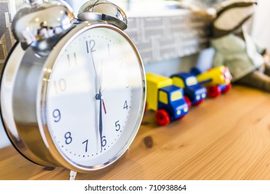 Closeup Of Modern Twin Bell Ring Analogy Clock On Wooden Table Desk Nightstand With Toy Trucks In Boy's Bedroom In Model House, Home Or Apartment