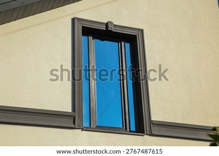 Close-up of a modern window with dark frame on a light textured wall, highlighting clean lines and minimalist architectural exterior design.