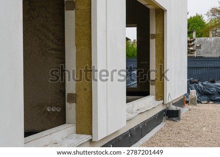 Close-up of modular prefab house facade with exposed mineral wool insulation around window openings