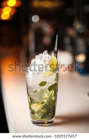 Close-up mojito cocktail with lemon and mint on the bar, blurred background.