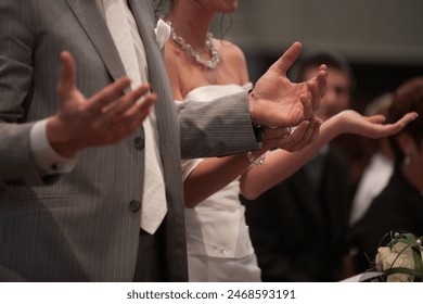 A closeup moment of a bride and groom joining hands to pray at a wedding ceremony in a church backdrop - Powered by Shutterstock