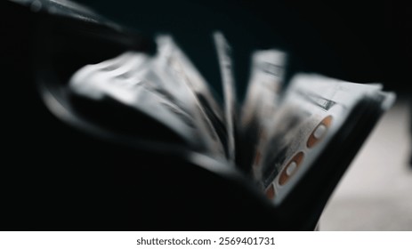Close-up of a money counting machine sorting hundred dollar bills against a dark background symbolizing wealth, capitalism and investment. Emphasis on currency and economic growth. 