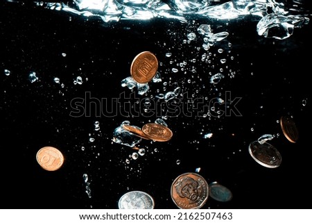 Close-up of money sinking in water. Treasure underwater. Gold and silver coins sink in the sea. Coins under water on a black background.
Sinking money is a sign of a weak economy.