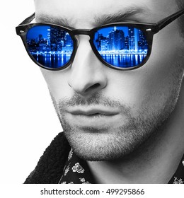 Closeup Monochrome Portrait Of Stylish Man In Sunglasses With Colorful Reflection. Modern City Skyscrapers In Lights At Night Reflected In Glasses. Concept Dream, Night Life, Success, Entertainment