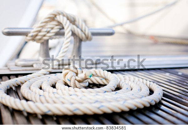 Close-up of a mooring\
rope with a knotted end tied around a cleat on a wooden pier/\
Nautical mooring rope