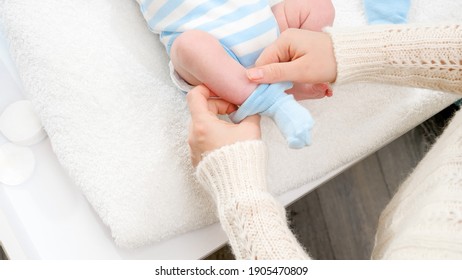 Closeup of mother dressing her little newborn baby son and putting on blue socks on tiny feet. Concept of babies and newborn hygiene and healthcare. Caring parents with little children