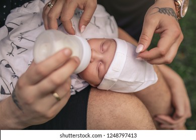 Closeup Of A Mother And Father Feeding Their Adorable Baby Boy With A Formula Bottle While Sitting Outside 