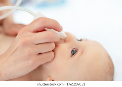 Closeup Mother Hand With Aspirator Medical Tool Cleaning Runny Nose Of Cute Infant Newborn Baby Boy Son At Home Indoors. Baby Parent Health Care And Love Concept