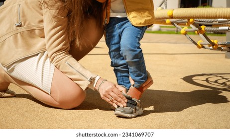 Closeup of mother putting on shoes to her baby son outdoors. Children playing outdoor, kids outside, summer holiday and vacation