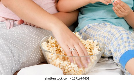 Closeup Of Mother And Son In Pajamas Taking Popcorn From Big Glass Bowl While Watching Cartoons Or Movie In Bed. Concept Of Cheerful Children And Family Happiness