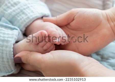 Close-up of a mother's hands cradling the feet of her newborn Caucasian child. The impact of demographic changes, birth rate and mortality