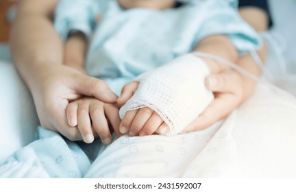 Closeup a mother's hands holds her little son's hands with saline line in hospital for treatment healthcare and rest on bed in hospital room from fever. - Powered by Shutterstock