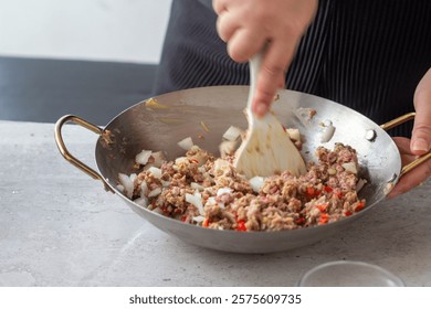 Close-up of motion hands using white spatula mixing ground meat with onions and spices in a wok

