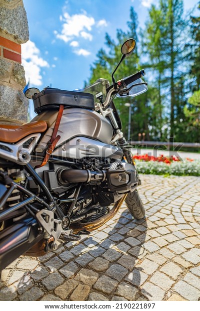 Closeup motorcycle parked on driveway road in warm\
sunny light. Blurred forest trees, park flowers and gravel stone\
road. Classic vintage motorbike, outdoor sport recreational\
pursuit. Nature travel