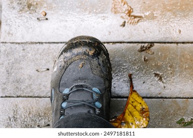 Close-up of a muddy hiking boot stepping on a wet wooden bridge, highlighting outdoor adventure in challenging conditions - Powered by Shutterstock