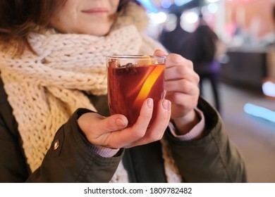 Close-up mug with mulled wine in woman hands, outdoor christmas evening market background