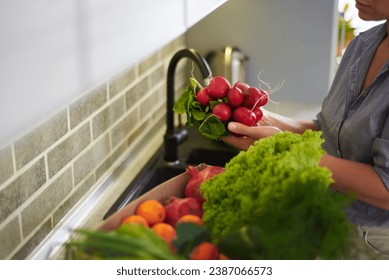 Close-up of a multi ethnic woman housewife, holding fresh radish, standing by kitchen counter with a cardboard box full of delivered fruits, vegetables and organic salad leaves. Healthy eating concept - Powered by Shutterstock