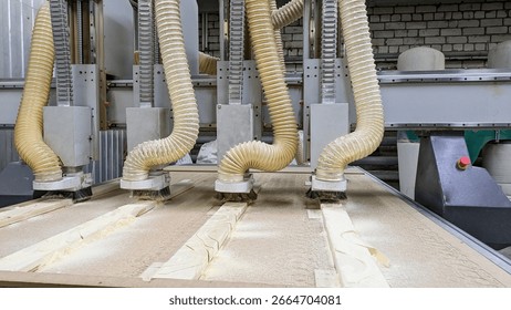 Close-up of multi-head CNC machine actively milling a workpiece, creating sawdust that is being collected by large corrugated pipes. Automated, high-precision process of modern woodworking