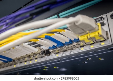 Closeup of multiple colored fiber optic LC connectors and network cables connected to 10G SFP plus switch ports in a professional data center server rack